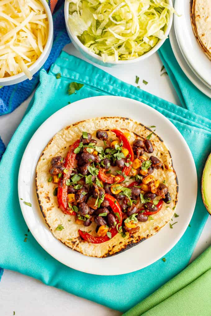 Taco with black beans and vegetables and bowls of toppings nearby