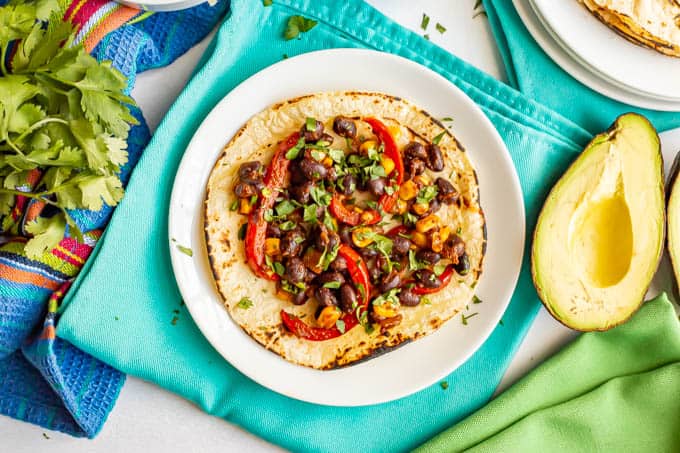 Vegetarian tacos with black beans, peppers and corn and cilantro and avocado nearby