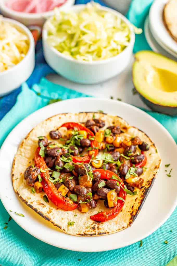 Black bean and bell pepper mixture on top of a tortilla shell with toppings in bowls in the background