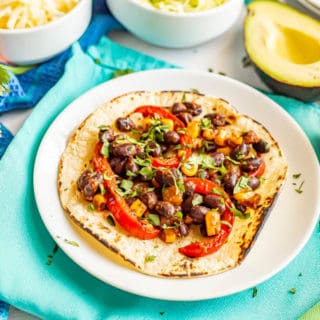 Black beans, corn and bell peppers on a taco shell with cilantro and avocado nearby