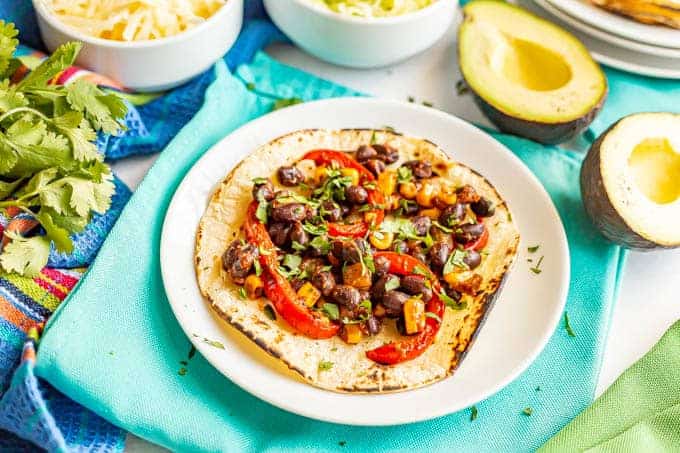 Black beans, corn and bell peppers on a taco shell with cilantro and avocado nearby