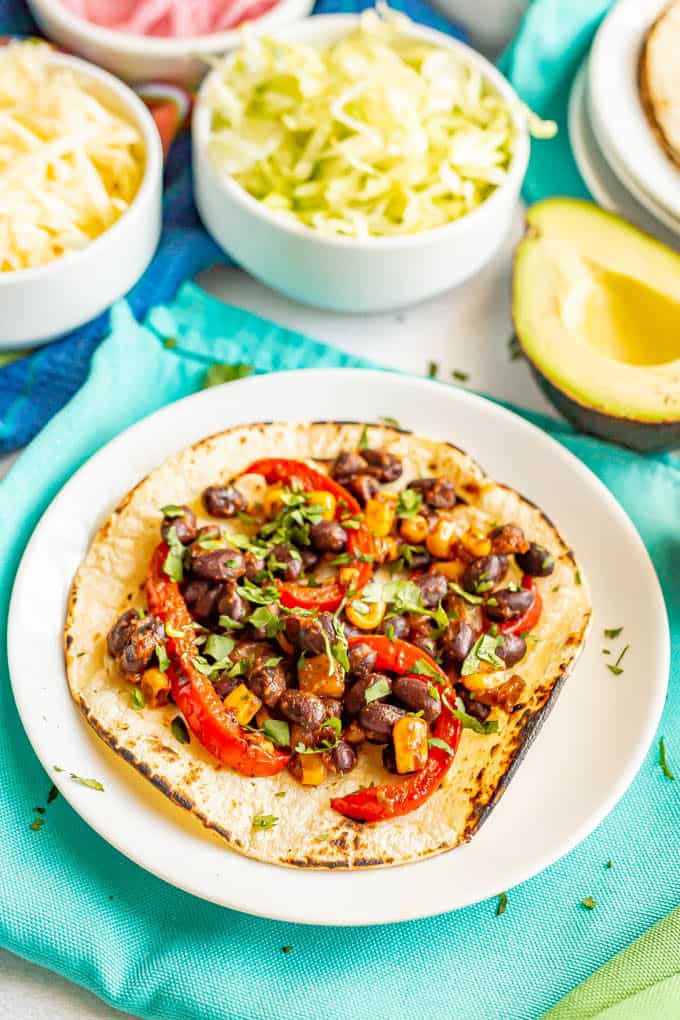 Black bean and bell pepper mixture on top of a tortilla shell with toppings in bowls in the background