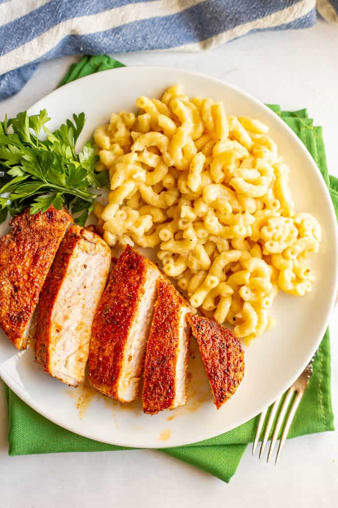 Seasoned cooked pork chops sliced and served with macaroni and cheese on a white plate on top of green napkins