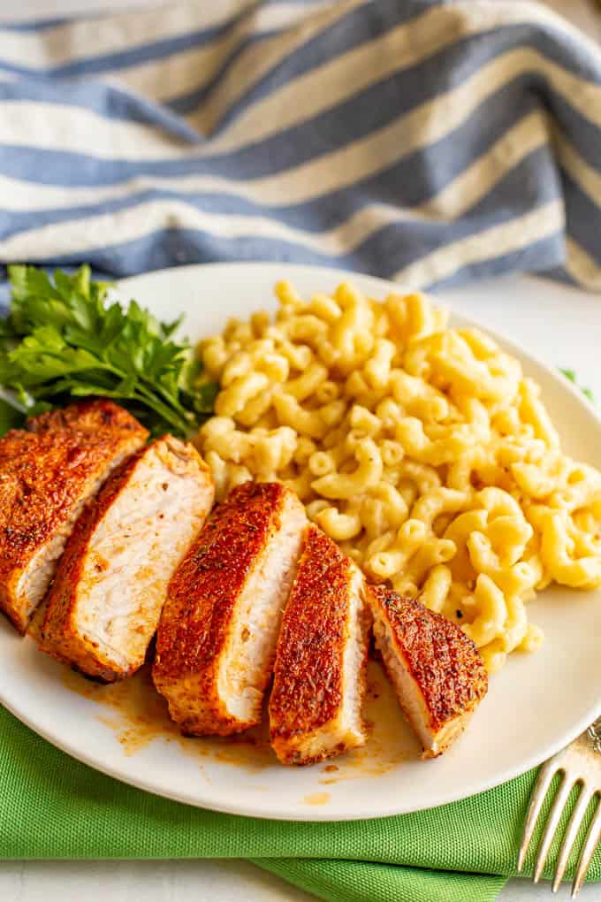 Thickly sliced pork chops served on a white plate with mac and cheese