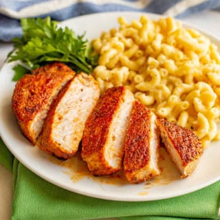 Sliced seasoned pork chop served on a white plate with mac and cheese and a parsley garnish