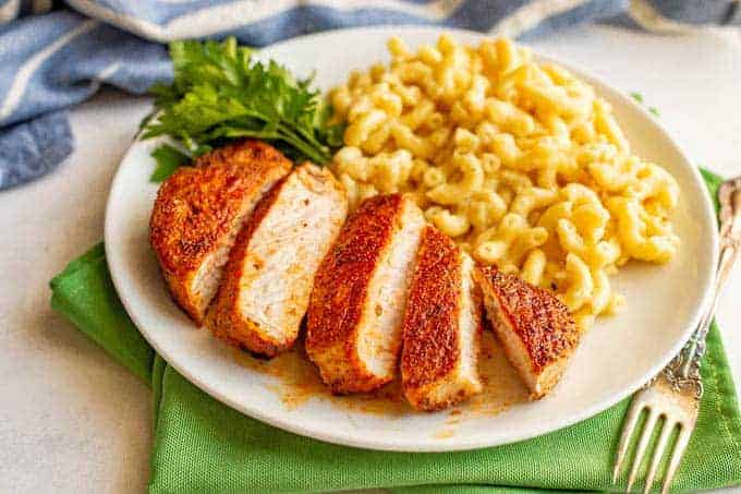 Sliced seasoned pork chop served on a white plate with mac and cheese and a parsley garnish