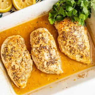 Seared and baked chicken breasts in a lemon sauce in a casserole dish with a bunch of parsley tucked in
