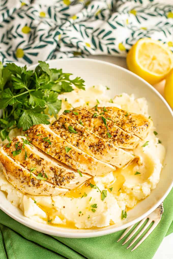 Sliced lemon chicken served over mashed potatoes in a large bowl with a lemon butter sauce and parsley over top