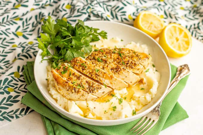 Sliced lemon chicken served over mashed potatoes in a large bowl with a lemon butter sauce and parsley over top