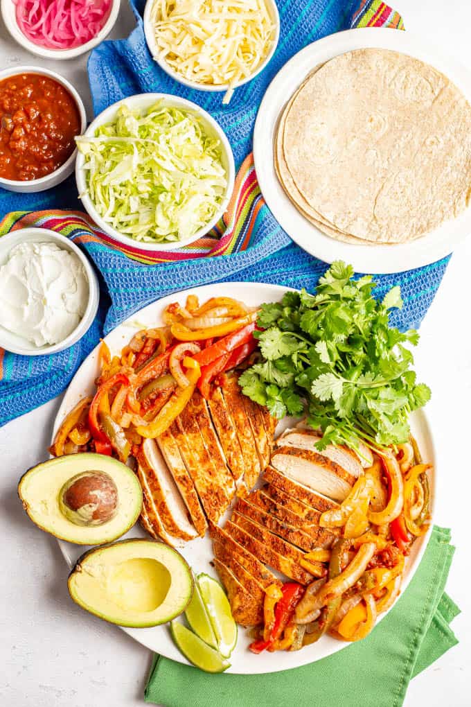 A large white serving platter piled with slow cooker chicken fajitas plus garnishes and bowls of toppings nearby