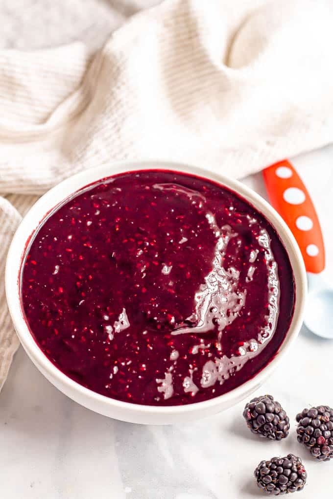 A bowl full of pureed blackberries with a baby spoon nearby