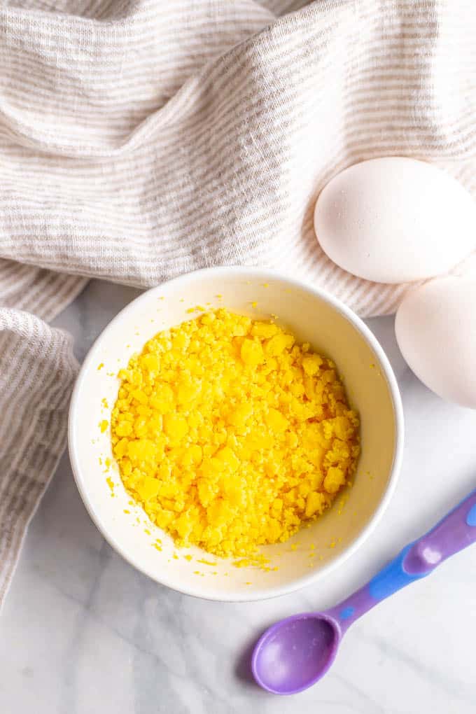 Mashed egg yolks in a small white bowl with a baby spoon nearby