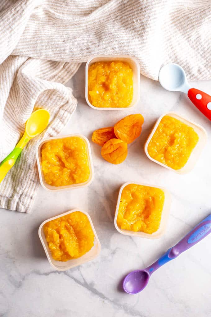 Homemade apricot puree in small containers with baby spoons nearby