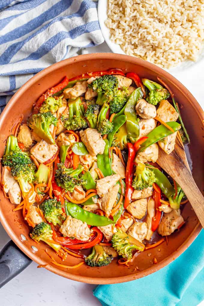 Honey garlic chicken stir fry with colorful vegetables in a large copper skillet with a bowl of rice nearby