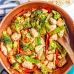 Chicken and vegetable stir fry with honey garlic sauce in a large saute pan with a wooden spoon resting in it