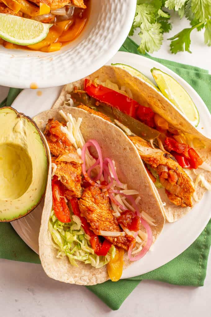 A couple of fajitas on a plate in flour tortillas with chicken and toppings