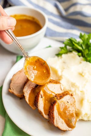 Gravy being drizzled over sliced pork tenderloin on a plate with mashed potatoes