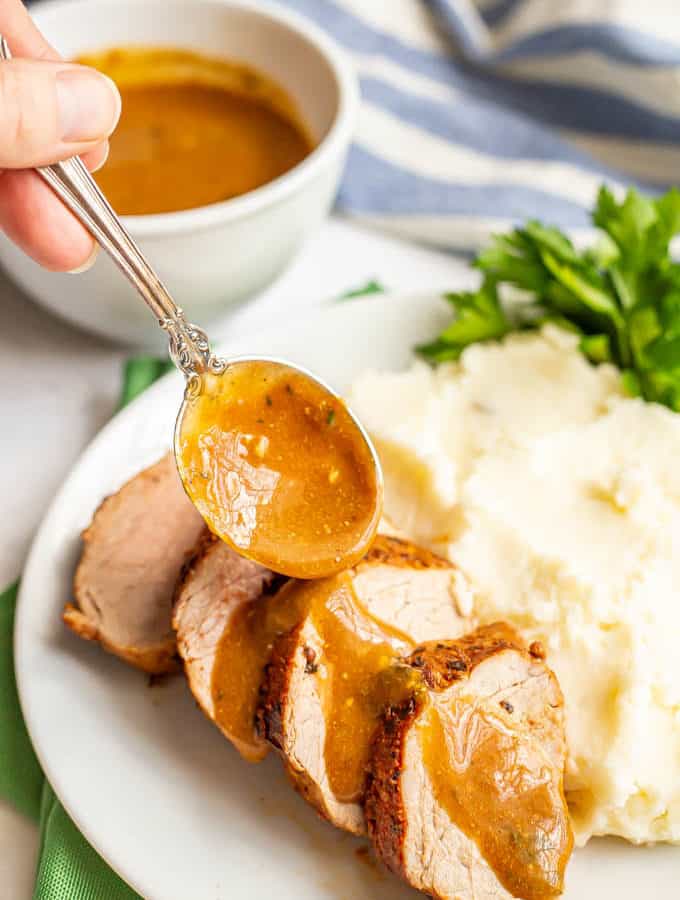 Gravy being drizzled over sliced pork tenderloin on a plate with mashed potatoes