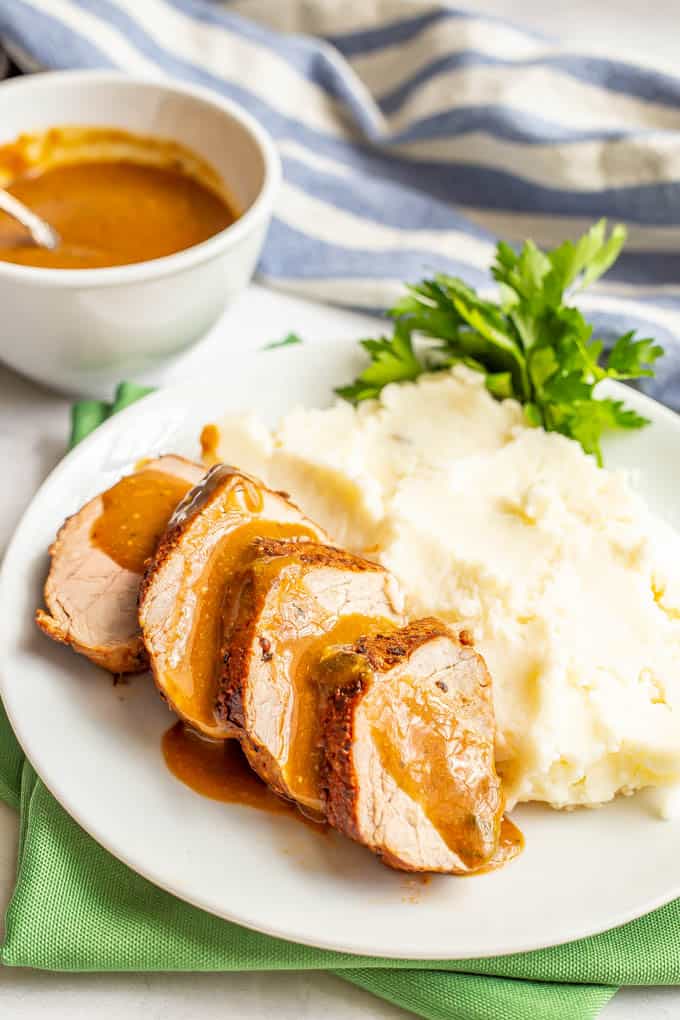 Sliced pork with gravy on a white plate with mashed potatoes