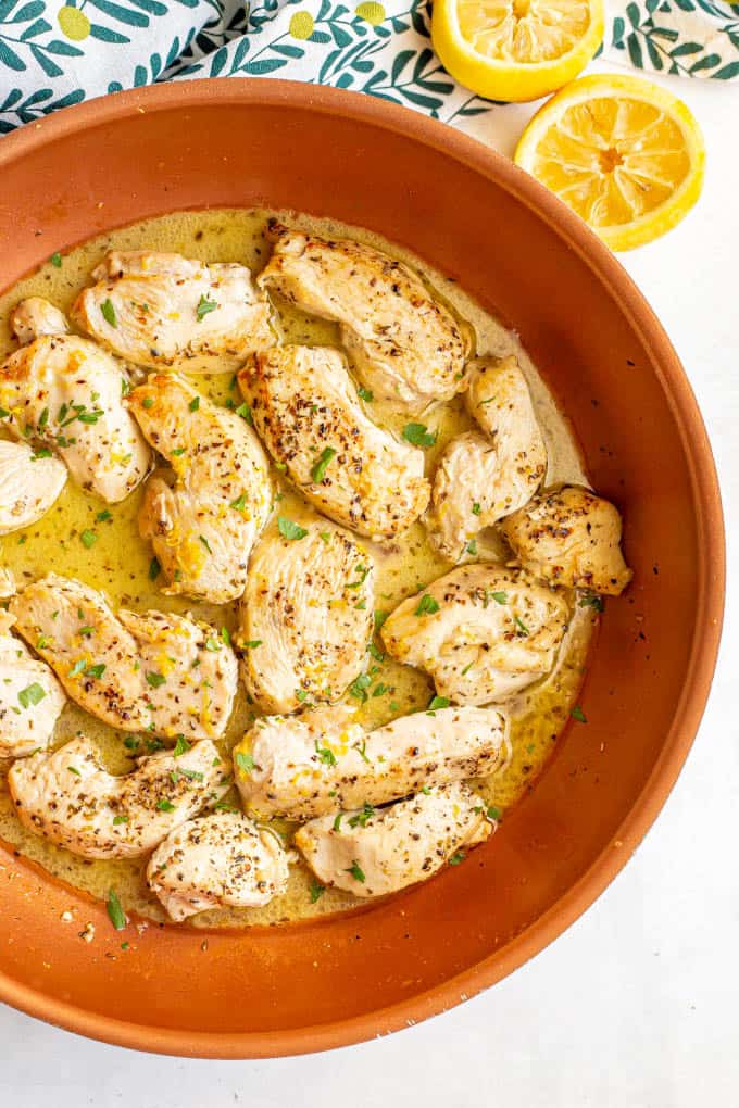 Seasoned, cooked chicken in a lemon sauce in a copper skillet with used lemon halves nearby