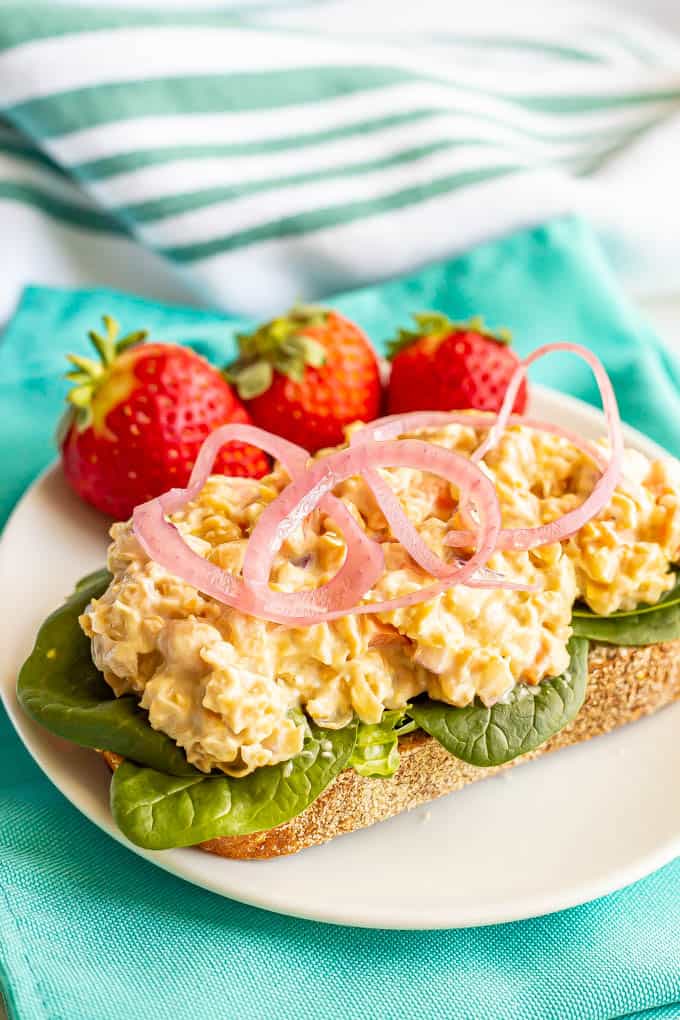 Chickpea salad piled onto a piece of toast with spinach and pickled red onions on a white plate