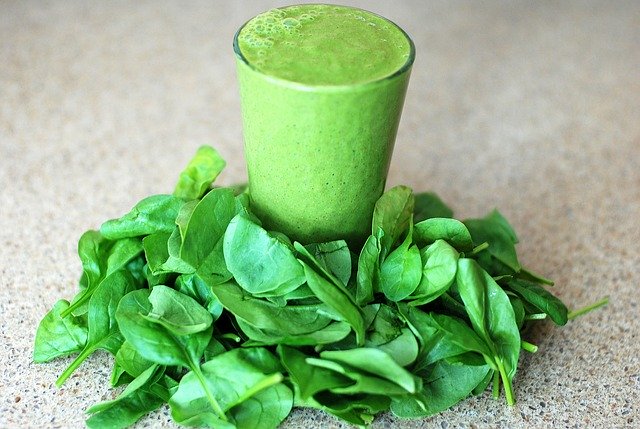 A pile of fresh baby spinach leaves around a full glass of green smoothie