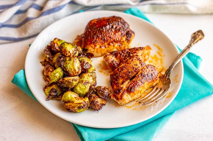 Sliced chicken thighs on a dinner plate with roasted Brussels sprouts and a fork