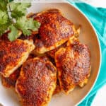 Seasoned baked chicken thighs served in a large white bowl with a sprig of parsley