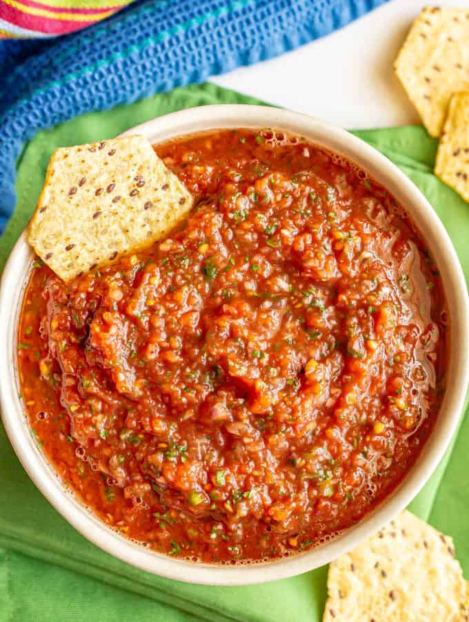 A bowl of homemade salsa with cilantro and jalapeno with a chip for dipping on the side