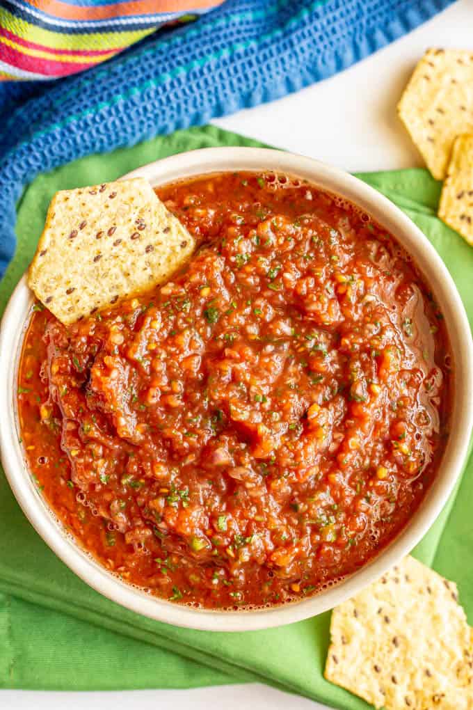 A bowl of homemade salsa with cilantro and jalapeno with a chip for dipping on the side