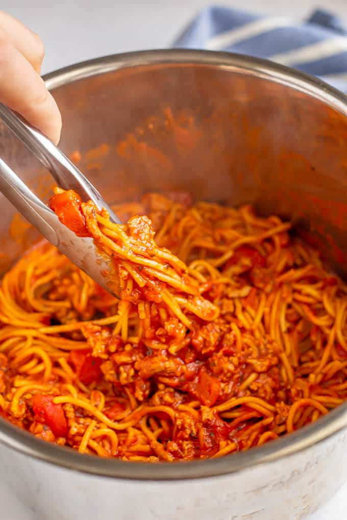 Cooked Instant Pot spaghetti with a hand pulling up tongs with twisted noodles