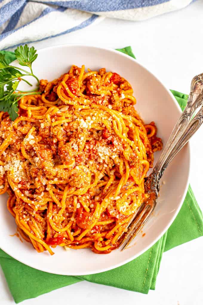 A white bowl of spaghetti with meat sauce and two forks on the side