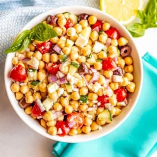 A colorful chickpea salad with tomatoes, cucumbers, olives and onions with a sprig of basil