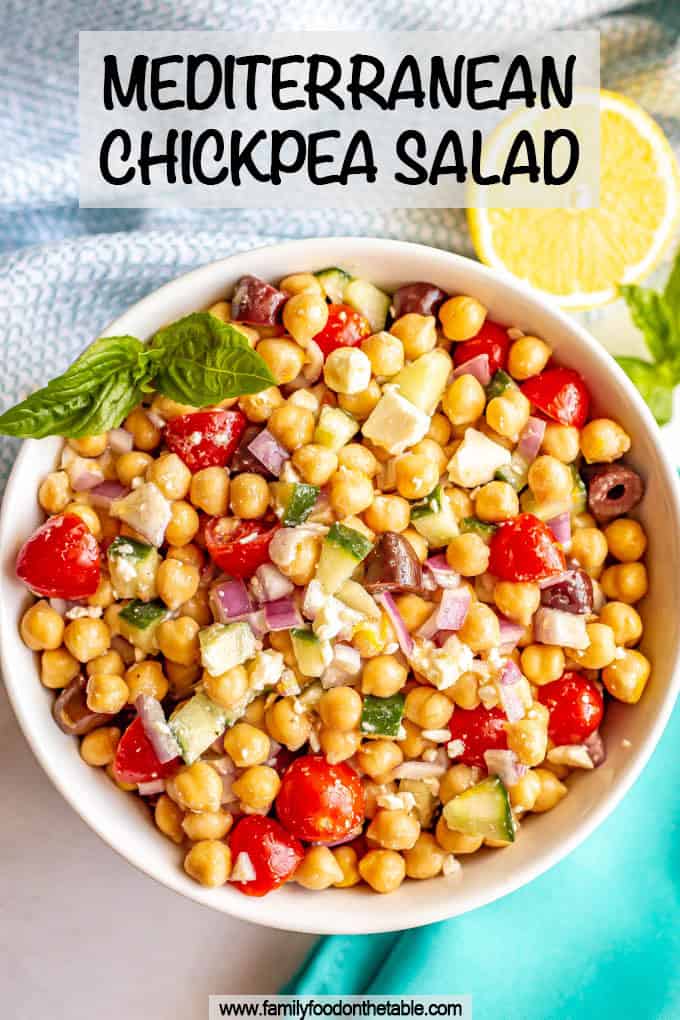 A colorful bowl of chickpea salad with tomatoes, cucumbers, olives and onions with a sprig of basil and a text box on top