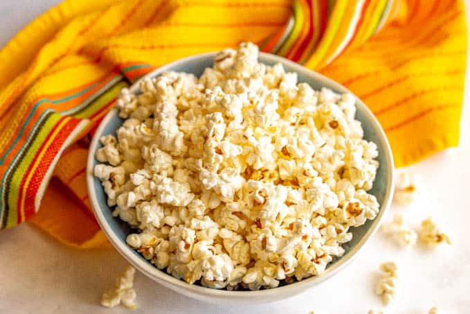 Microwave popped popcorn served in a large blue and white bowl with popcorn scattered on the table and a yellow hand towel