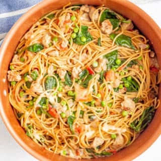 A large copper pot filled with spaghetti noodles, chicken sausage, spinach and peas