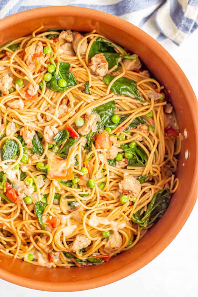 A large copper pot filled with spaghetti noodles, chicken sausage, spinach and peas