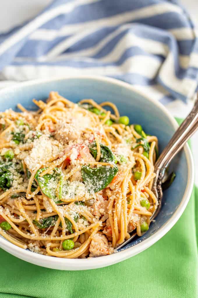 A blue and white bowl of pasta with chicken sausage, spinach and peas and Parmesan cheese on top with two forks resting in the bowl