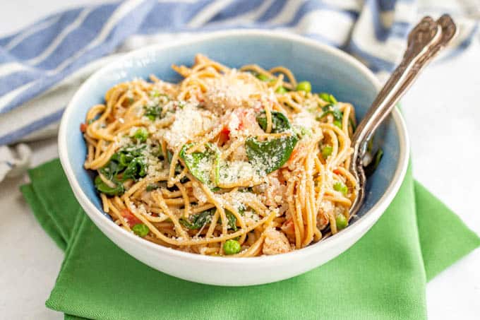 A blue and white bowl of pasta with chicken sausage, spinach and peas and Parmesan cheese on top