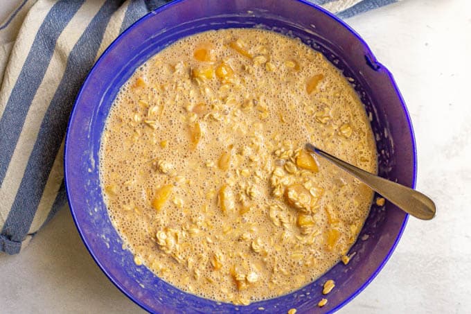 A blue mixing bowl with an oat batter mix with peaches