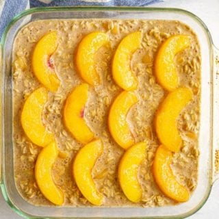 A square glass baking dish with an oatmeal mixture topped with peach slices