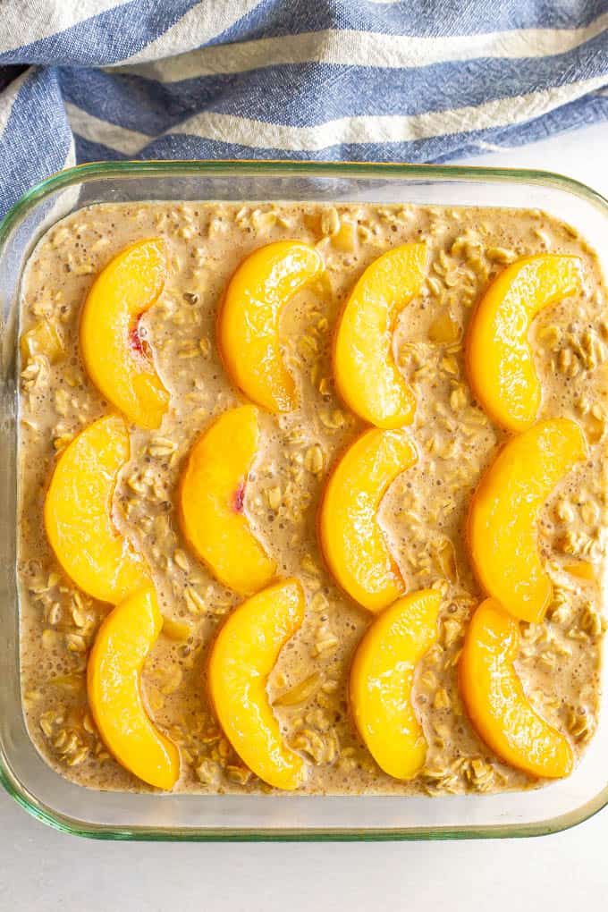 A square glass baking dish with an oatmeal mixture topped with peach slices before being baked
