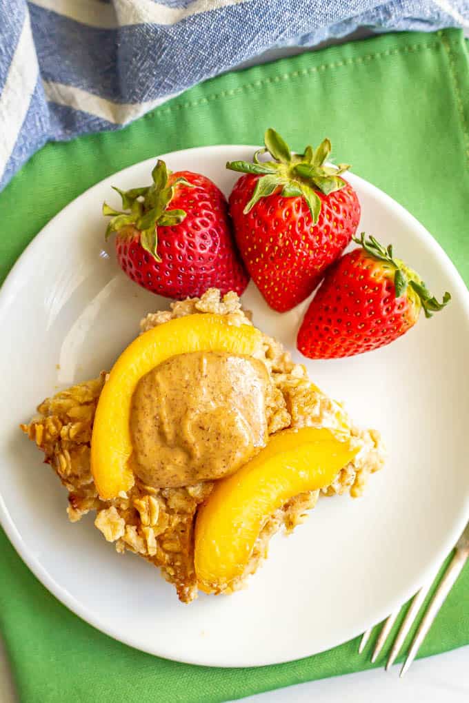 A slice of baked oatmeal with peaches and almond butter served on a plate with strawberries