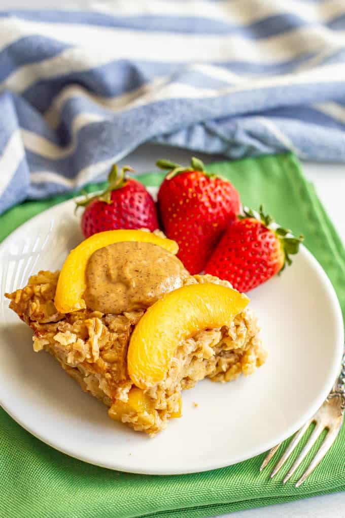 A slice of baked oatmeal with peaches and almond butter served on a plate with strawberries