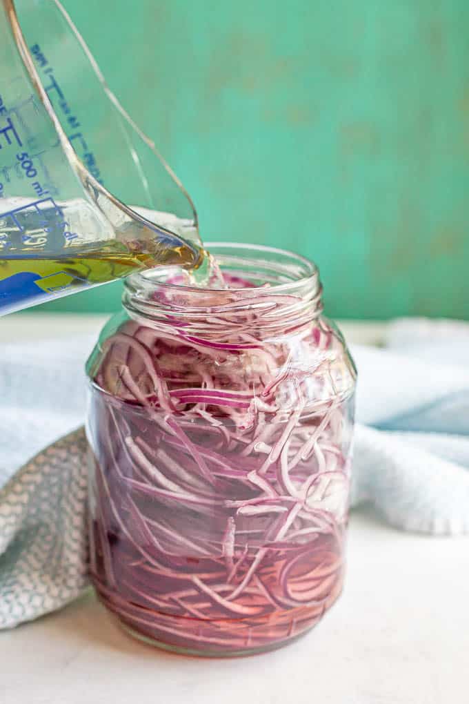 A vinegar mixture being poured into a glass jar of sliced red onion