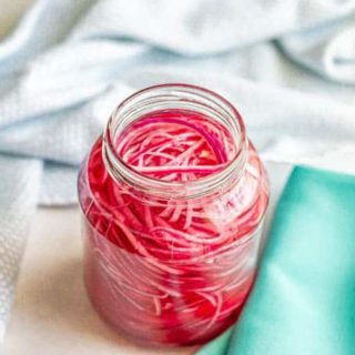 A glass jar of pickled sliced red onions with turquoise napkins beside the jar