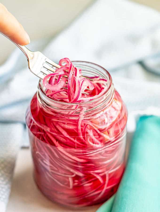 A fork lifting up a few strands of red onion from a jar
