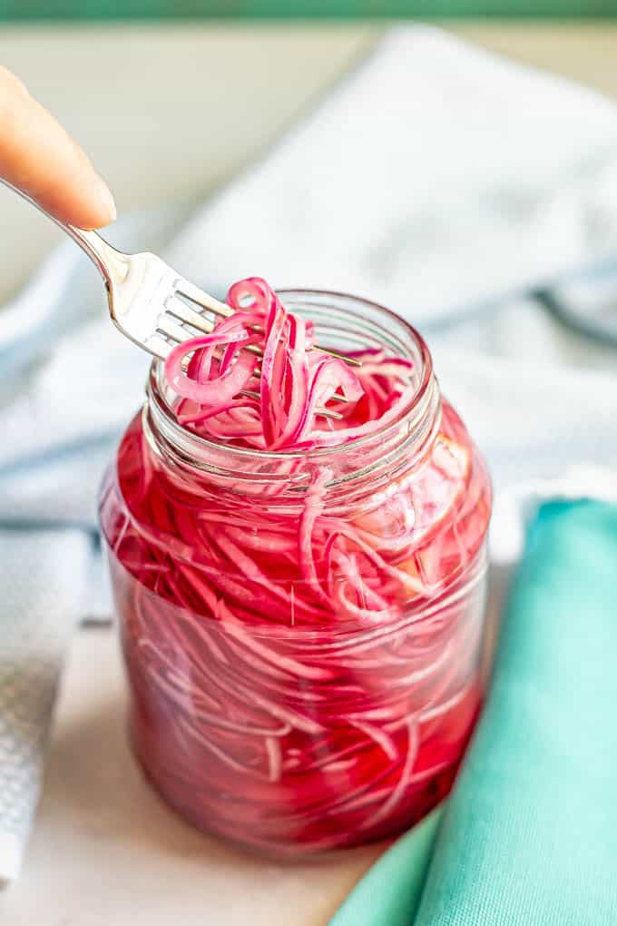 A fork lifting up a few strands of red onion from a jar
