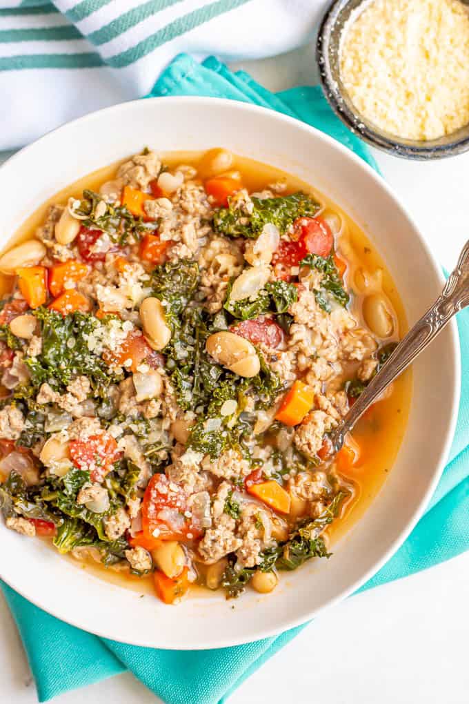 Kale turkey soup with white beans and veggies served with a spoon and a bowl of Parmesan