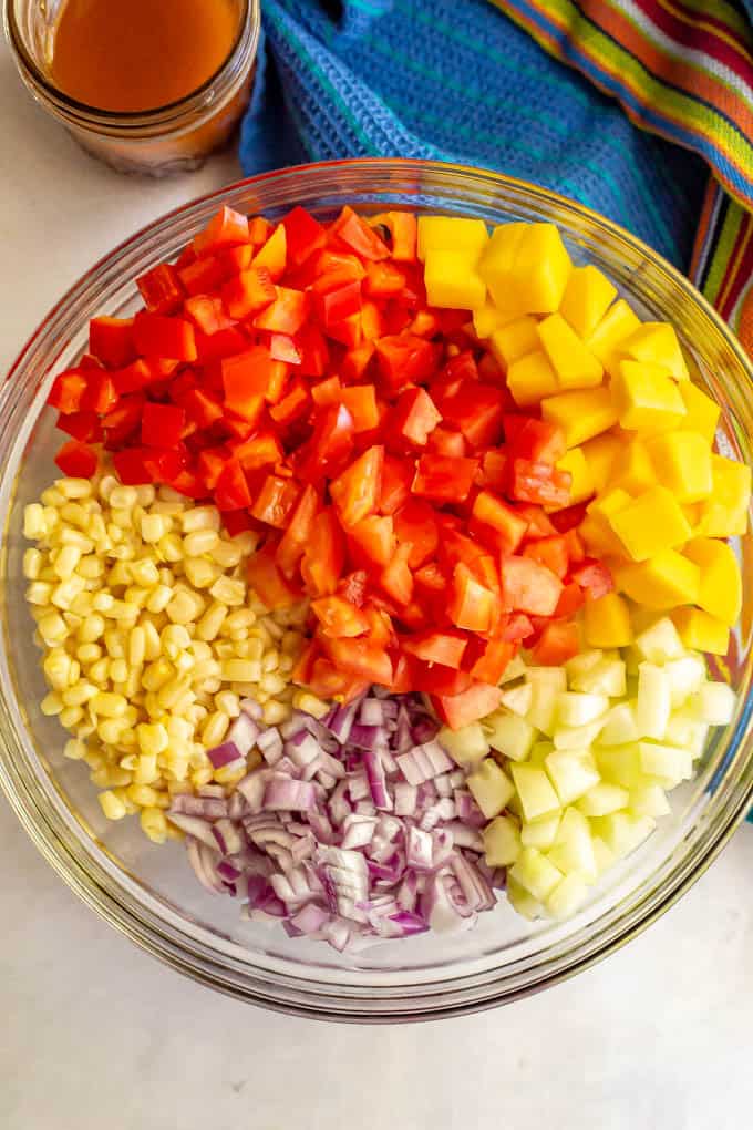 Fresh veggies arranged in a large clear glass bowl before being mixed with a jar of dressing nearby